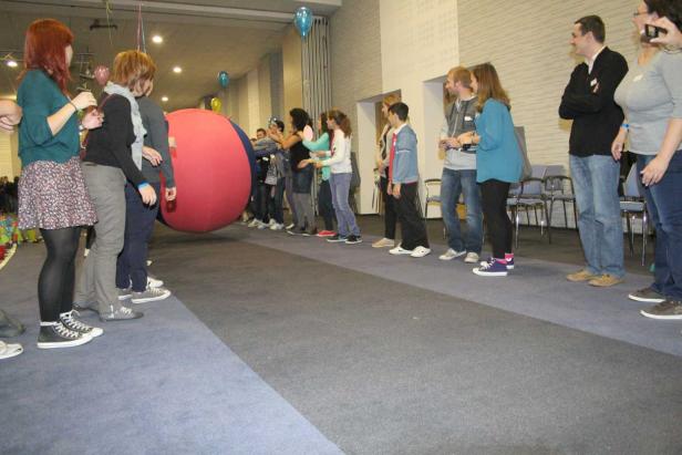 Eine Gruppe von Menschen steht in einer Reihe und spielt mit einem großen, roten Ball.