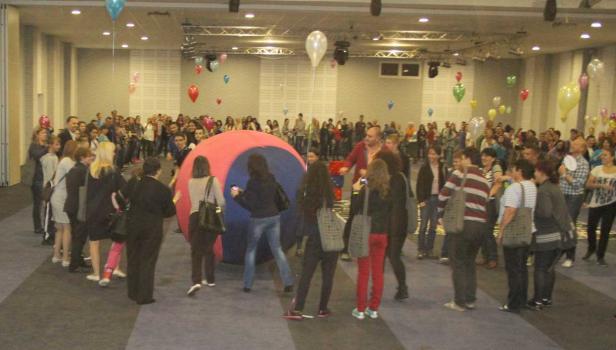 Eine Menschenmenge steht um eine große, aufblasbare Kugel in einem Raum mit Ballons.