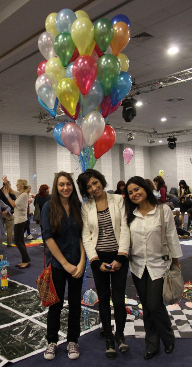 Drei Frauen posieren vor einem bunten Ballonstrauß in einem großen Raum.