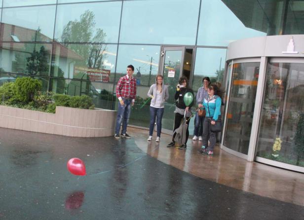 Eine Gruppe junger Leute steht vor einem modernen Gebäude mit einem roten Ballon.