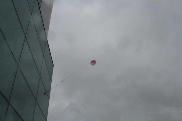 Ein roter Ballon steigt vor einem grauen Himmel auf.