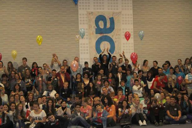 Eine große Gruppe von Menschen sitzt und steht vor einem Banner mit Ballons.