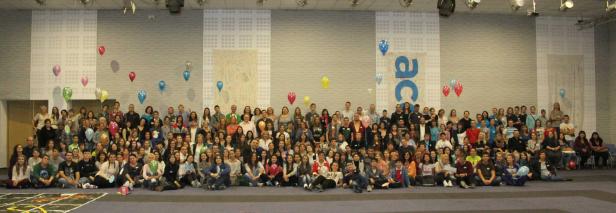 Eine große Gruppe von Menschen posiert für ein Gruppenfoto mit bunten Ballons im Hintergrund.