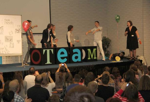 Eine Gruppe von Menschen steht auf einer Bühne hinter großen Blöcken, die das Wort „TEAM“ bilden.