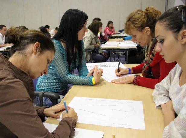 Mehrere Frauen sitzen an Tischen und füllen Arbeitsblätter aus.