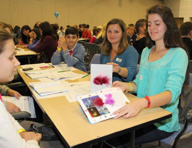 Schüler und Lehrer sitzen an Tischen und präsentieren Bastelarbeiten.