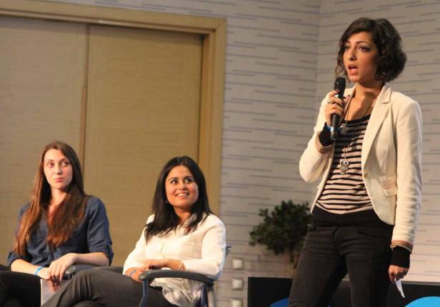 Eine Frau spricht bei einer Podiumsdiskussion in ein Mikrofon, während zwei weitere Frauen sitzen.