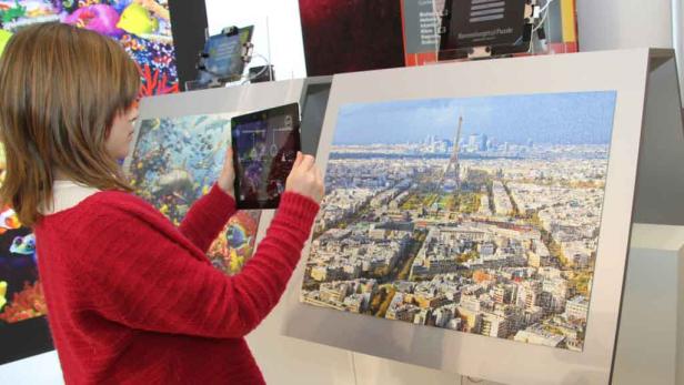 Eine Frau betrachtet ein Puzzle mit einem Luftbild von Paris und dem Eiffelturm durch ein Tablet.