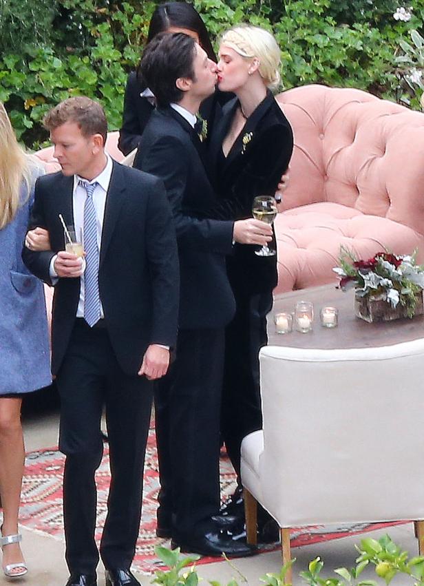 Ein Paar in formeller Kleidung küsst sich im Freien bei einer Feier.