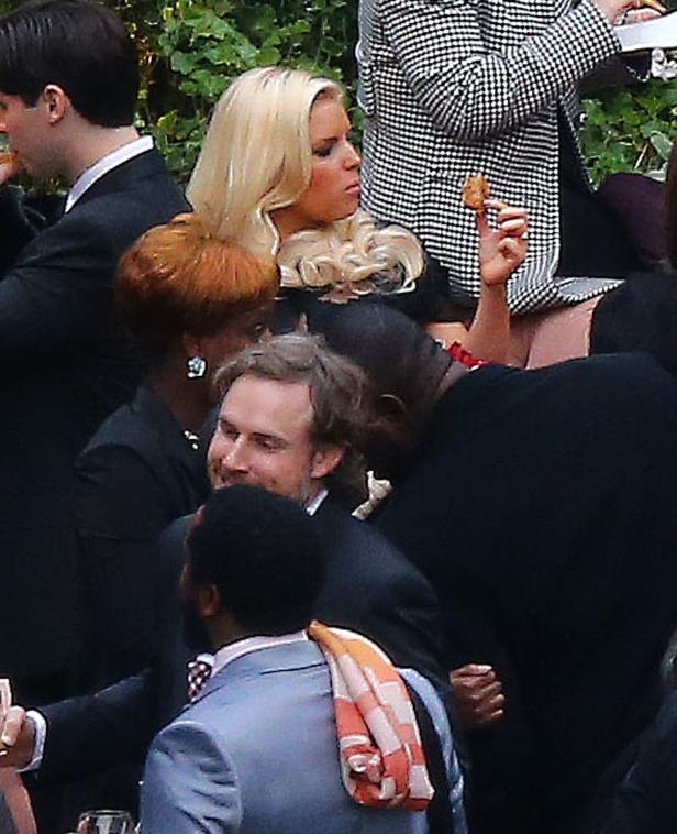 Eine blonde Frau isst inmitten einer Gruppe von Menschen einen kleinen Snack.