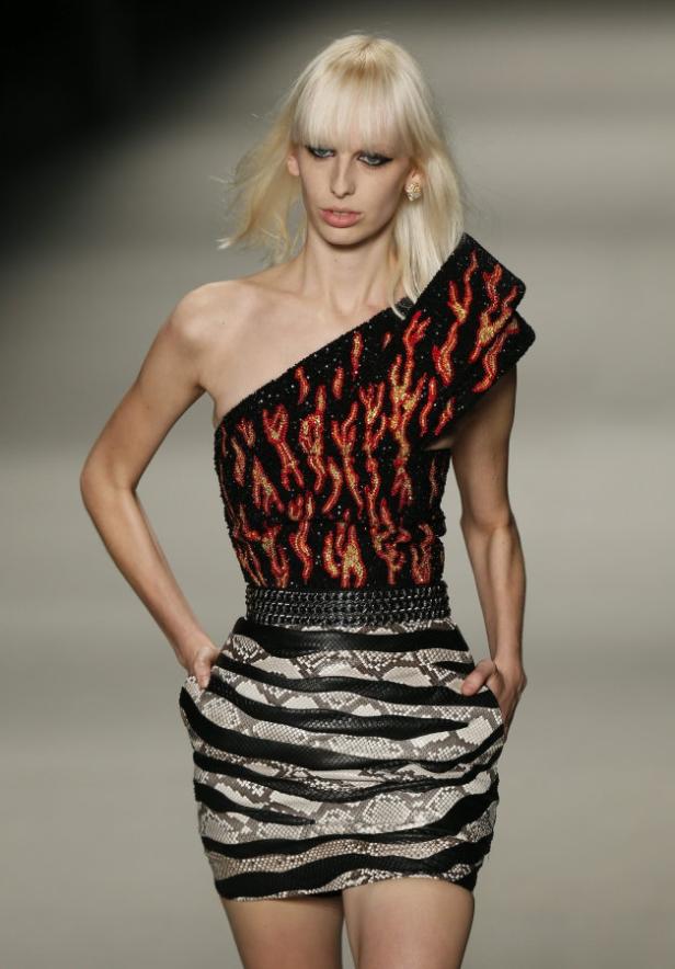 Ein Model präsentiert ein schulterfreies Kleid mit Flammenmuster und Schlangenlederrock.