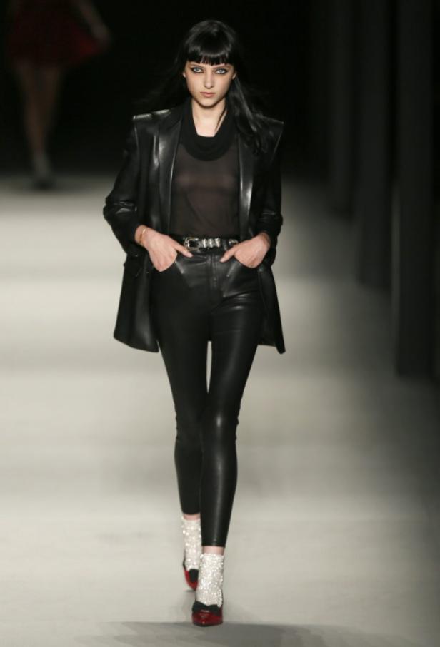 Eine Frau mit Pony trägt ein schwarzes Lederoutfit auf einem Laufsteg.