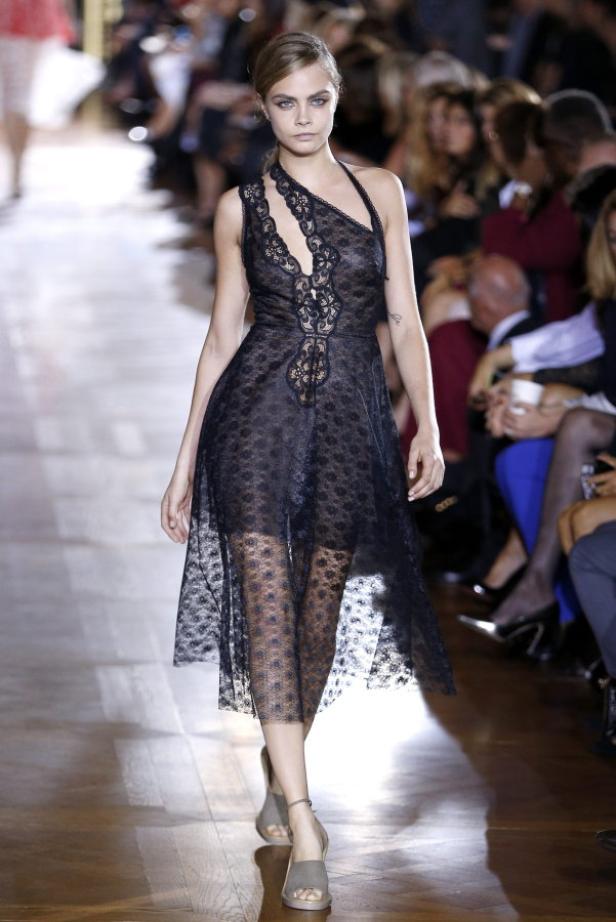 Cara Delevingne läuft in einem schwarzen Spitzenkleid über einen Laufsteg.