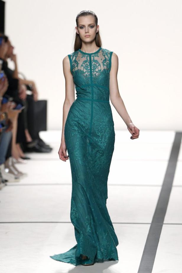 Ein Model präsentiert ein smaragdgrünes, bodenlanges Spitzenkleid auf dem Laufsteg.