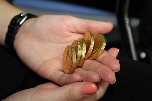 Eine Hand hält mehrere in Goldfolie verpackte Schokoladenmünzen.