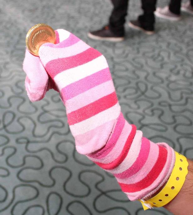 Eine Hand mit einem gestreiften Socken als Puppe hält eine goldene Münze.