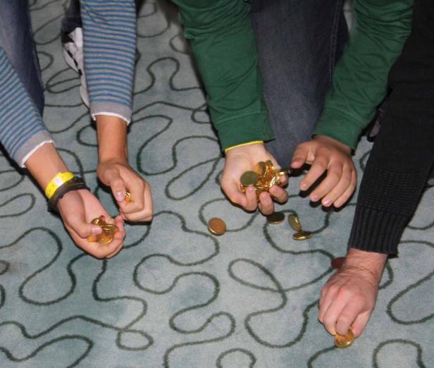 Mehrere Personen sitzen auf dem Boden und spielen mit goldenen Münzen.