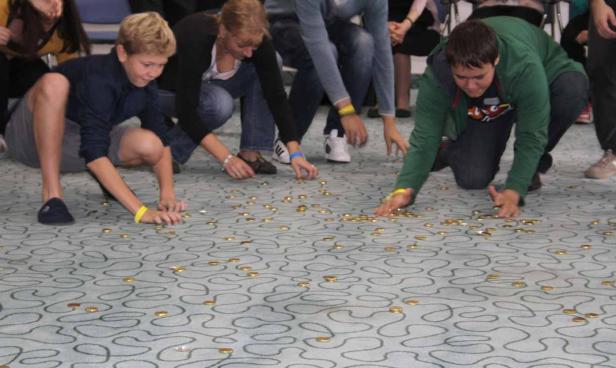 Mehrere Personen sammeln goldene Münzen vom Teppich auf.