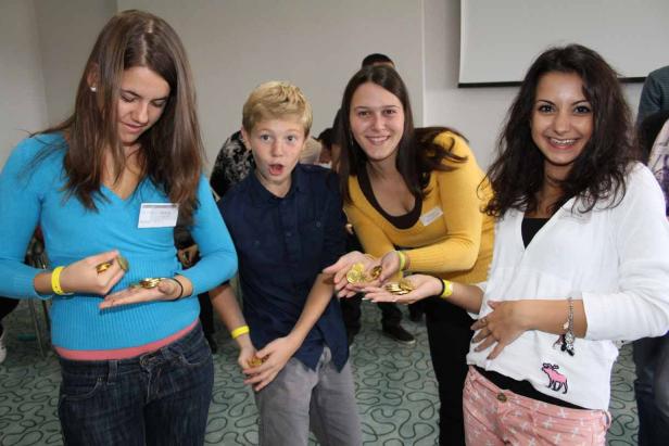 Vier junge Leute halten Goldmünzen in ihren Händen.