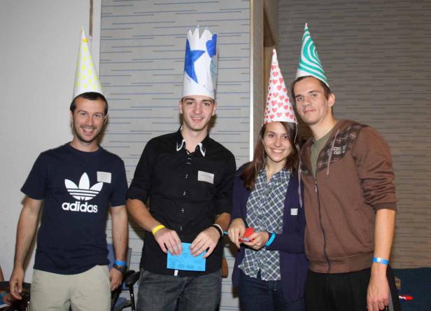 Vier junge Leute mit Partyhüten stehen nebeneinander und lächeln.