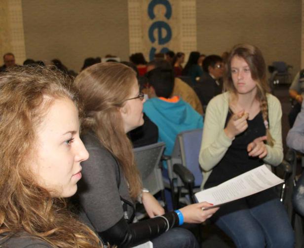 Drei junge Frauen sitzen in einem Publikum und unterhalten sich.