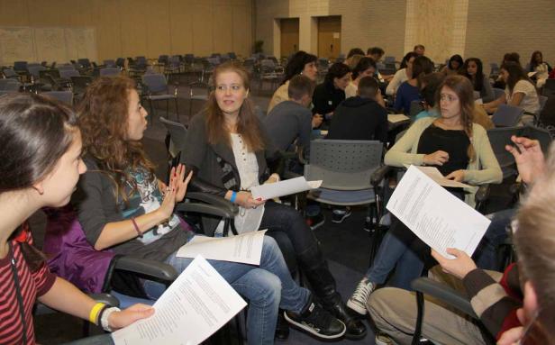 Eine Gruppe junger Leute sitzt in einem Raum und diskutiert mit Papier in der Hand.