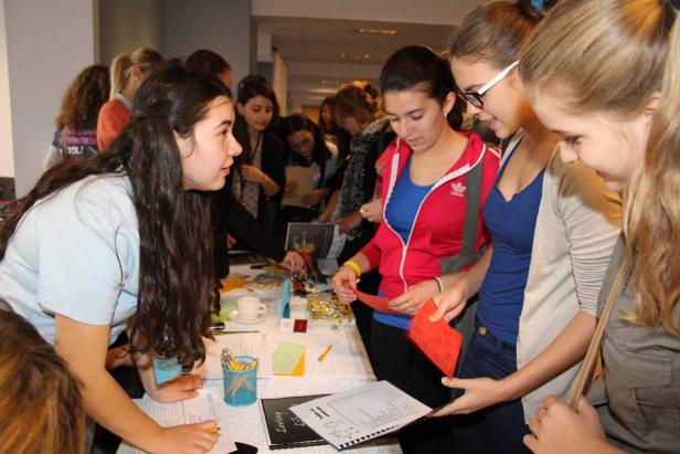 Eine Gruppe junger Frauen steht an einem Tisch und betrachtet Informationsmaterialien.