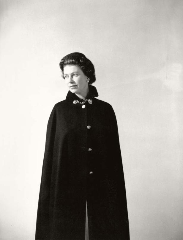 Königin Elizabeth II. trägt einen dunklen Umhang mit Knöpfen und einer Brosche.