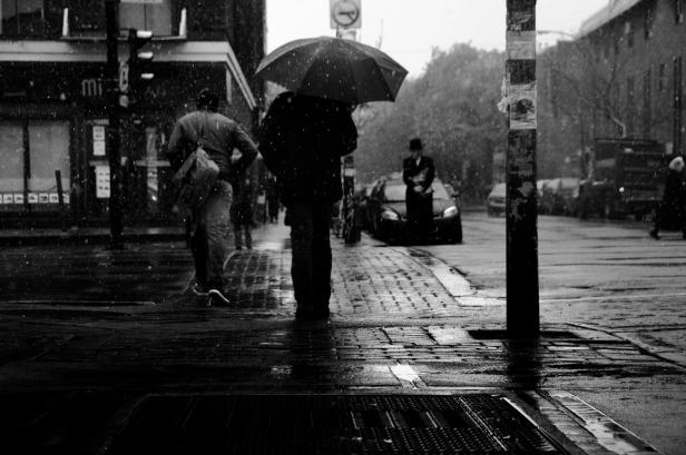 Ein regnerischer Tag in der Stadt, Menschen mit Regenschirmen eilen vorbei.