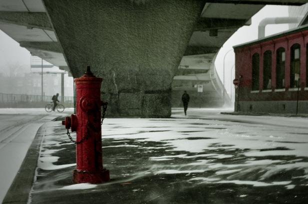 Ein roter Hydrant steht an einer verschneiten Straße unter einer Brücke.