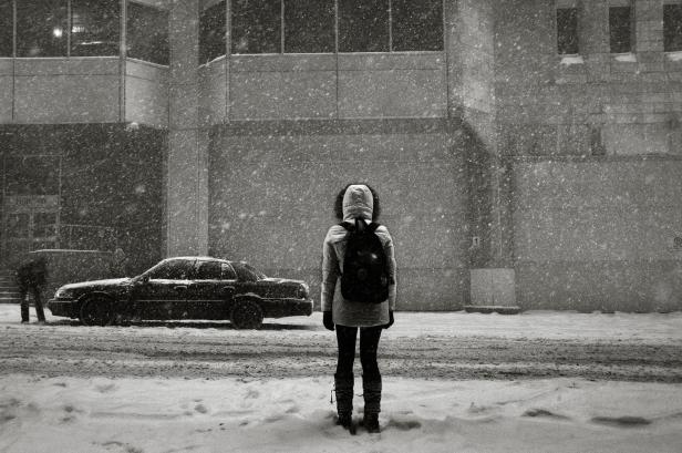 Eine Person mit Rucksack steht im Schneefall vor einem Gebäude.
