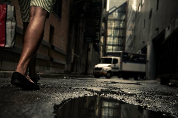Eine Person geht in einer dunklen Gasse an einer Wasserpfütze vorbei.