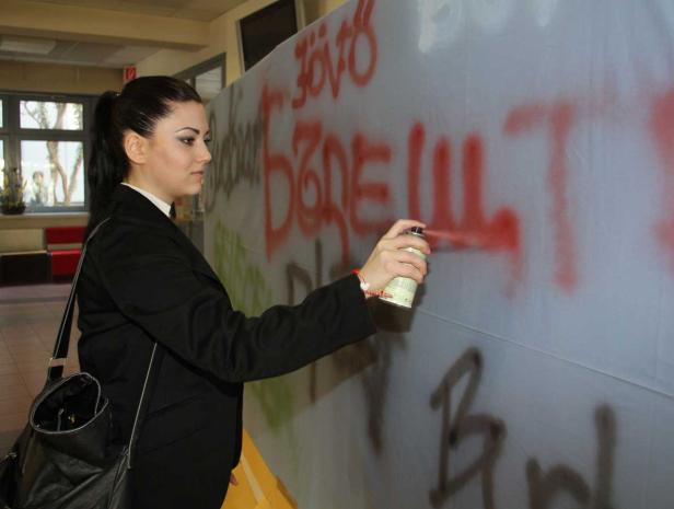 Eine Frau sprüht Graffiti auf eine Wand in einem Innenraum.