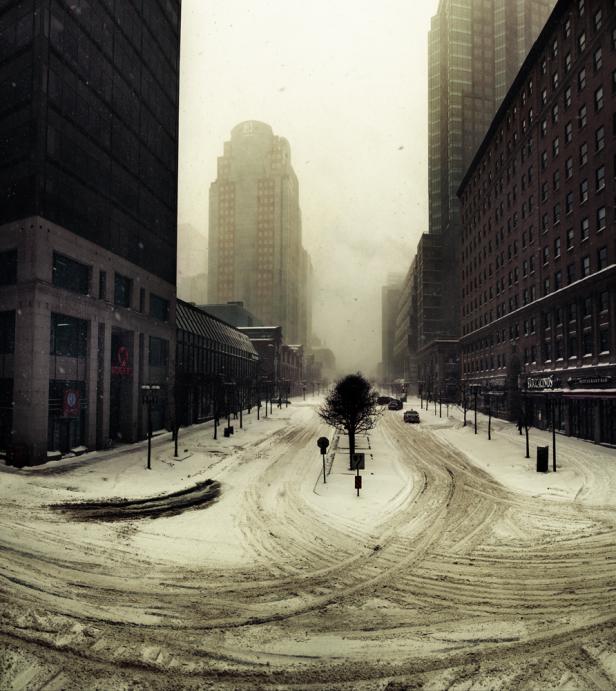 Eine verschneite Straße in einer Stadt mit hohen Gebäuden im Hintergrund.