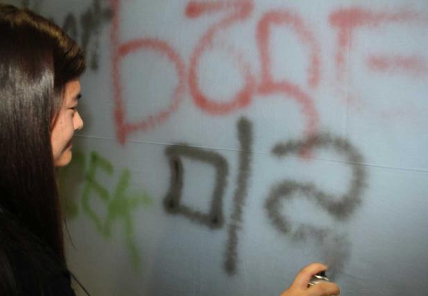 Eine junge Frau sprüht Graffiti auf eine Wand.