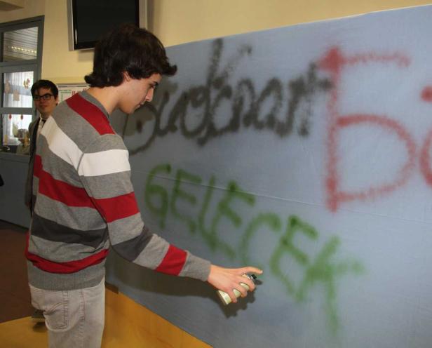 Ein junger Mann sprüht Graffiti auf eine blaue Plane.