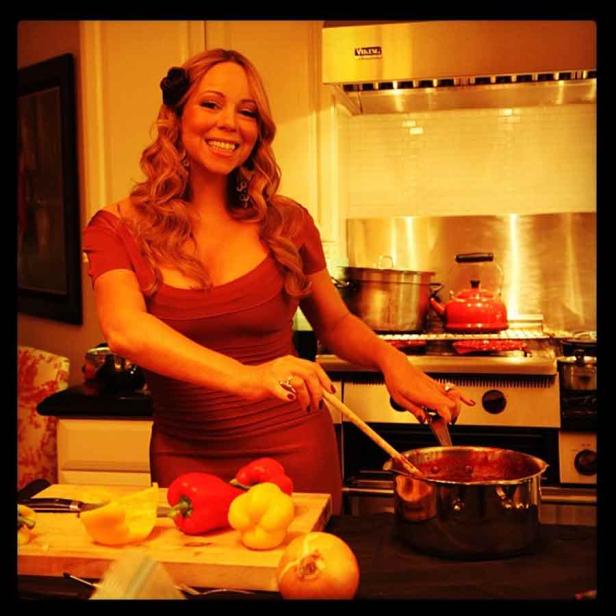 Mariah Carey rührt lächelnd mit einem Holzlöffel in einem Topf in ihrer Küche.