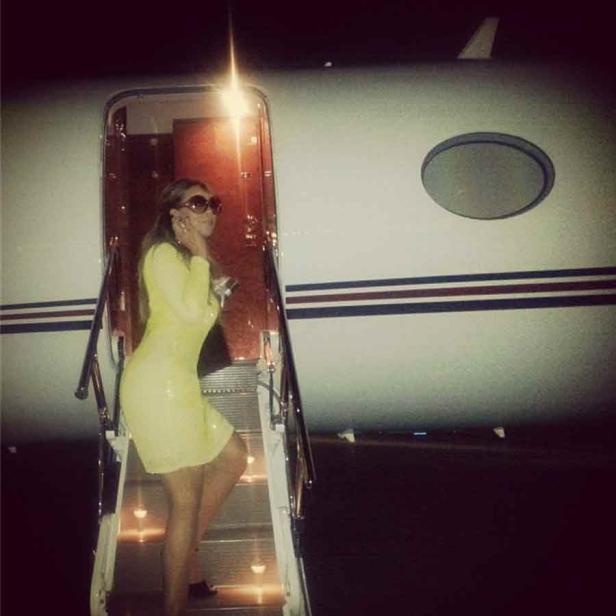 Eine Frau in einem gelben Kleid steigt die Treppe eines Privatjets hinauf.