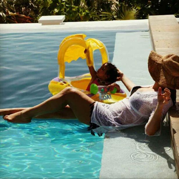 Eine Frau entspannt am Pool, während ein Kind in einem gelben Schwimmreifen spielt.