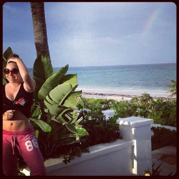 Eine Frau steht vor einer tropischen Landschaft mit Strand und einem Regenbogen am Himmel.