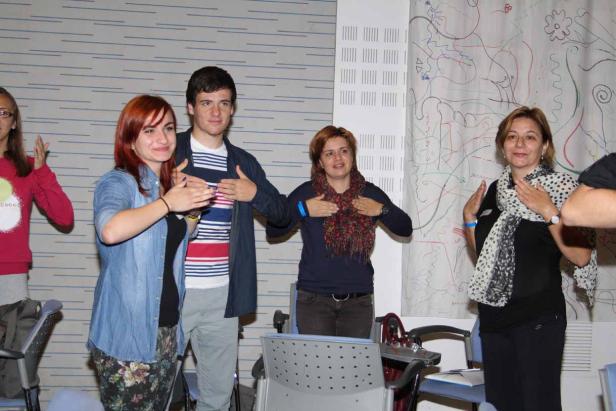 Eine Gruppe von Menschen steht in einem Raum und hält die Hände auf die Brust.