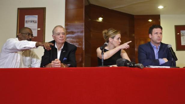 Vier Personen sitzen an einem Tisch mit roter Tischdecke und zeigen mit den Fingern in verschiedene Richtungen.