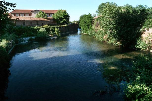 Ein ruhiger Flusslauf schlängelt sich durch eine ländliche Gegend mit alten Gebäuden.