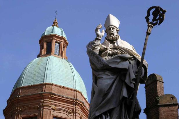 Eine Statue von Petronius von Bologna vor einer Kirche mit grüner Kuppel.
