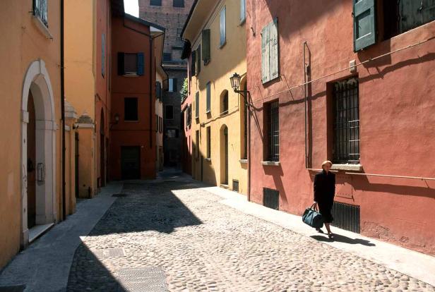 Eine Frau geht mit einer Tasche eine Gasse mit Kopfsteinpflaster entlang.
