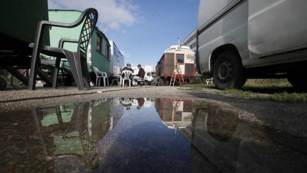 Eine Gruppe von Wohnwagen steht auf einem Platz, gespiegelt in einer Wasserpfütze.