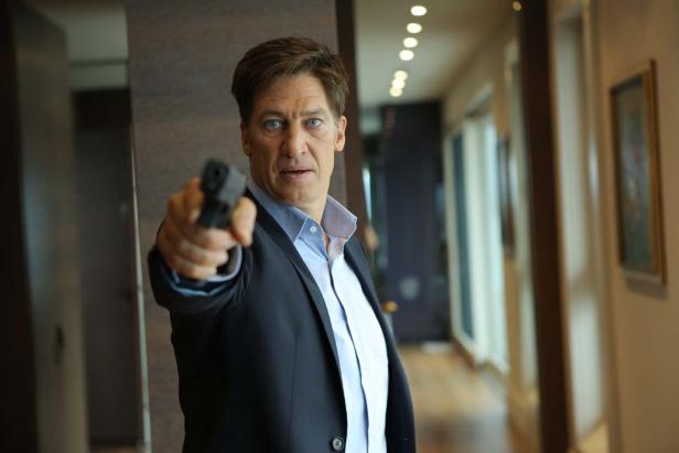 Ein Mann im Anzug zielt mit einer Pistole.