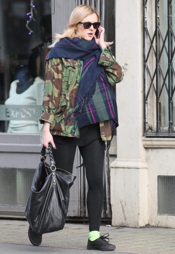 Eine Frau mit Sonnenbrille telefoniert auf der Straße und trägt eine Jacke im Camouflage-Stil.