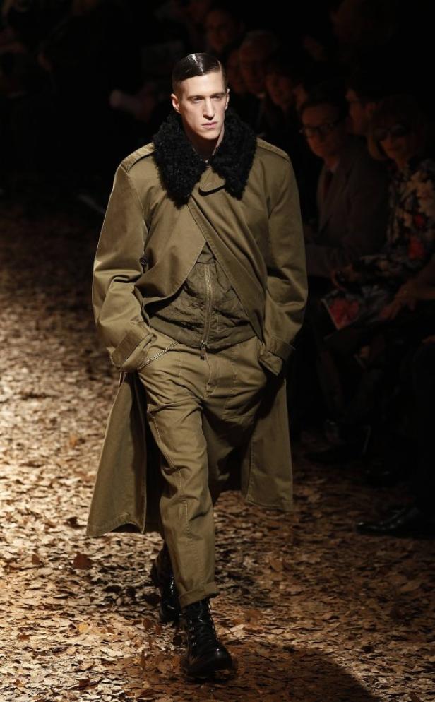 Ein Mann in einem olivgrünen Mantel mit Fellkragen auf einem Laufsteg.