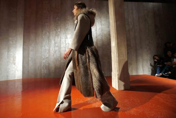 Eine Frau präsentiert einen Mantel mit Pelzbesatz auf einem orangefarbenen Laufsteg.